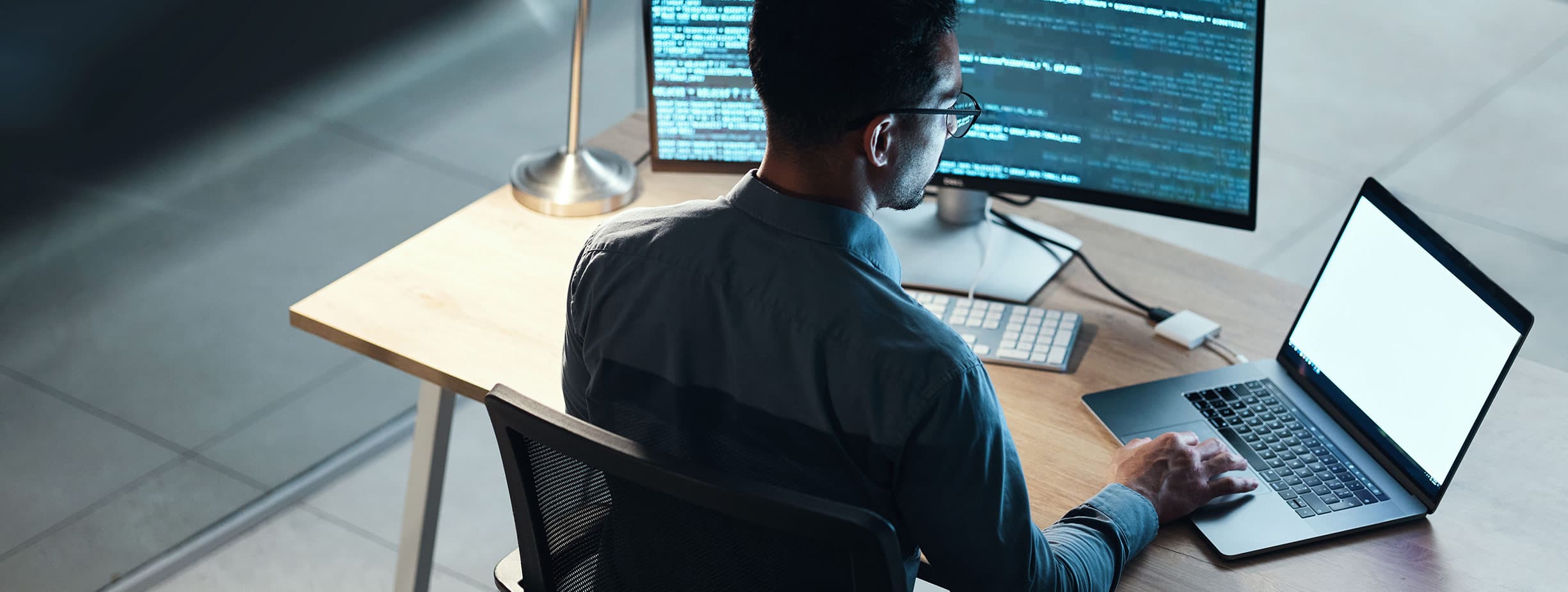 Close up of a cybersecurity analyst typing and working on a laptop, desktop computer and mobile phone.