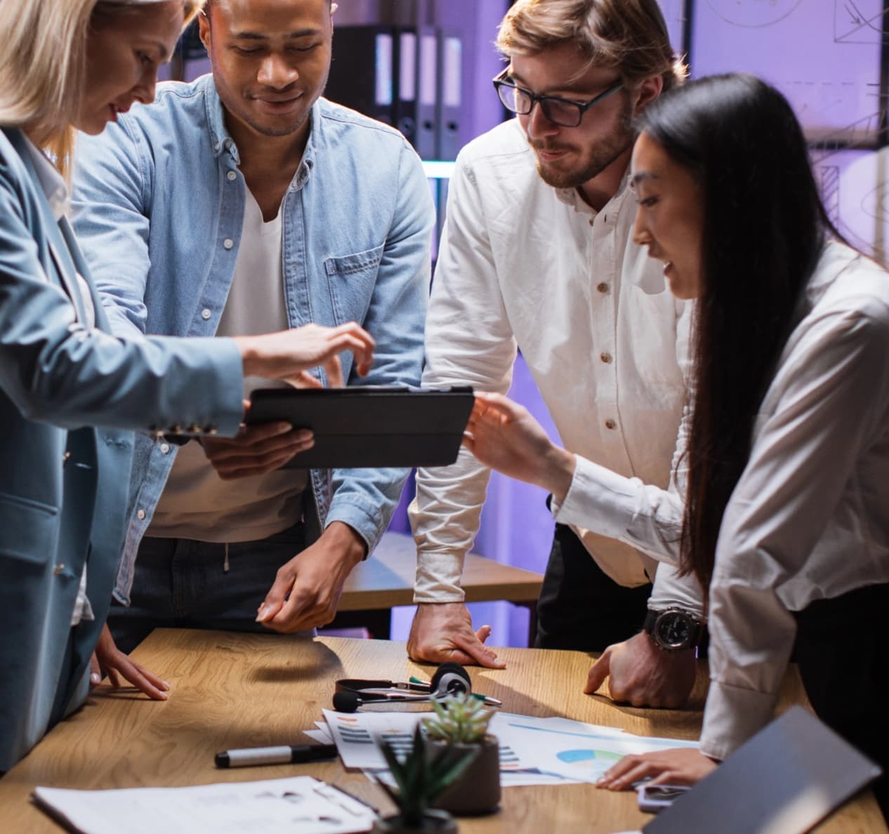 A team works collectively on a tablet over a table during a meeting